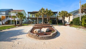 A beachfront property with a central landscaped area featuring rocks and palm trees, surrounded by multi-story buildings with balconies and a covered walkway.