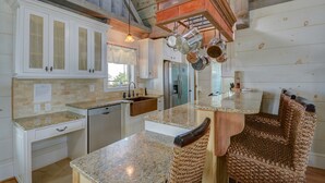 A kitchen with white cabinets, granite countertops, a wooden island, and woven chairs.