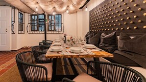 A dining area with a wooden table set for four, surrounded by black chairs. A black cushioned sofa is against the wall, and a decorative wall panel with circular indentations is visible. - Beaux-Arts house in Condesa with rooftop (Ciudad de México)