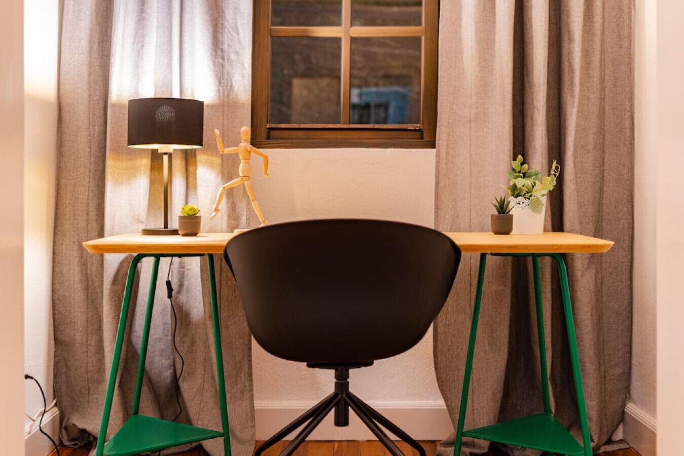 Et værelse med skrivebord, stol, lampe og et vindue med gardiner.