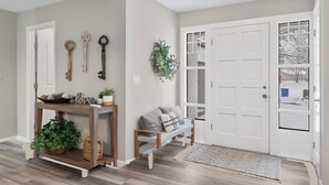 Un couloir avec une console en bois, un banc et une porte dotée de panneaux de verre.