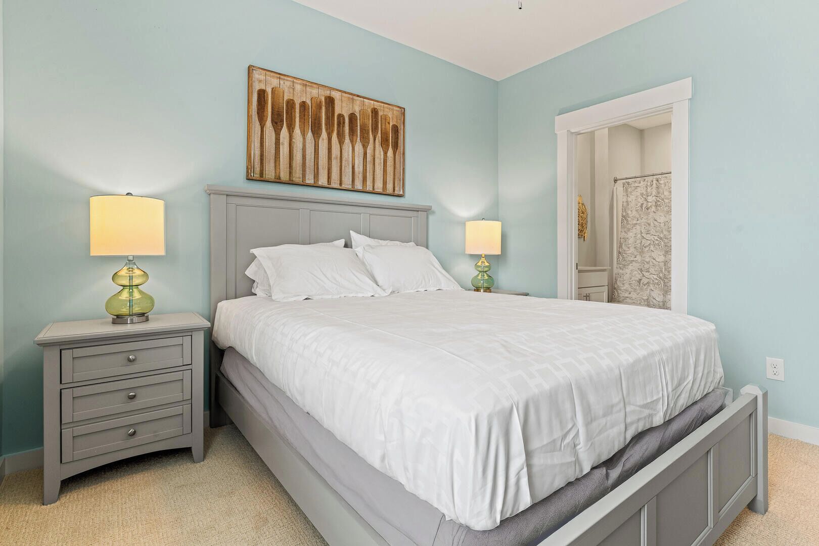A bedroom with a bed, two bedside tables with lamps, a headboard, and a wall-mounted artwork.