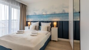 A hotel room with a large bed, two bedside tables, a nightstand, a painting of a sailboat on the sea, and a view of the city through the window. - Vacation apartment by the sea, vacation on the island of Usedom, Apartment BALTYCKI A22 (Świnoujście)