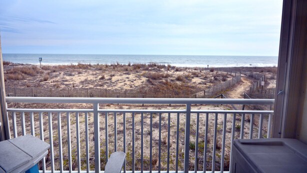 A balcony with a view of a sandy beach and the ocean.