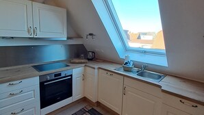 Cozinha compacta com armários brancos, forno embutido e janela com vista para uma área residencial.