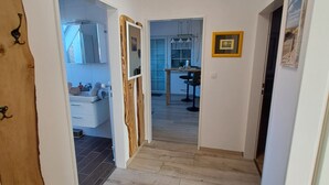 Um corredor com uma porta de madeira à esquerda, um tapete preto na entrada e uma luminária no teto.