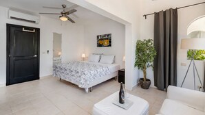 Een moderne slaapkamer met een bed, nachtlampjes, een plafondventilator, een potplant en een groot raam met gordijnen.