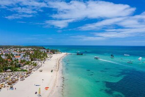 Una playa con aguas turquesas cristalinas, un muelle y una ciudad al fondo.
