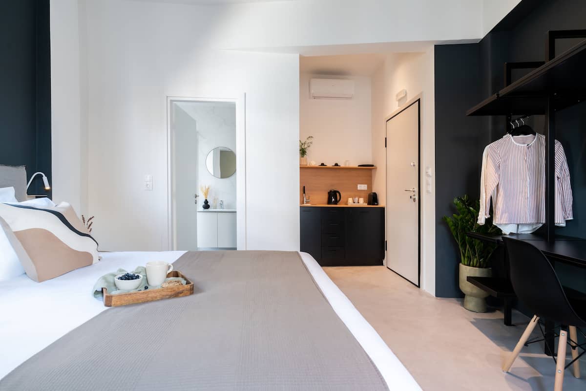 A modern hotel room with a large bed, a desk, a wardrobe, and a kitchenette.