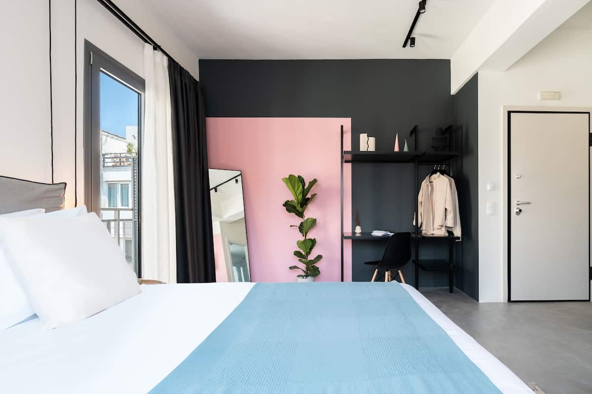 A modern hotel room with a bed, a desk, a wardrobe, and a potted plant.