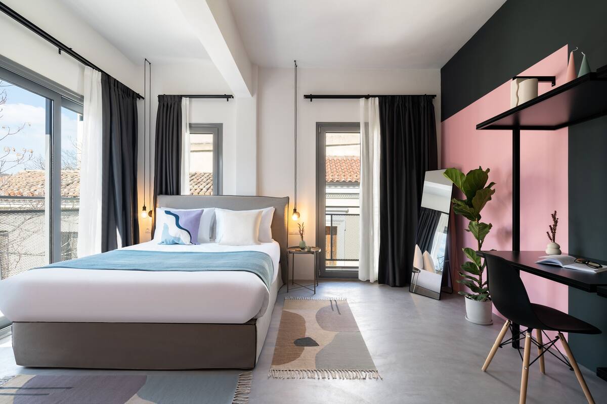 A modern bedroom with a large bed, a desk, and a potted plant.
