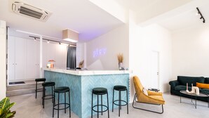 A modern kitchen with a bar area, bar stools, a sofa, and a neon sign. - Play Psyri, a member of Brown Hotels (Athens)