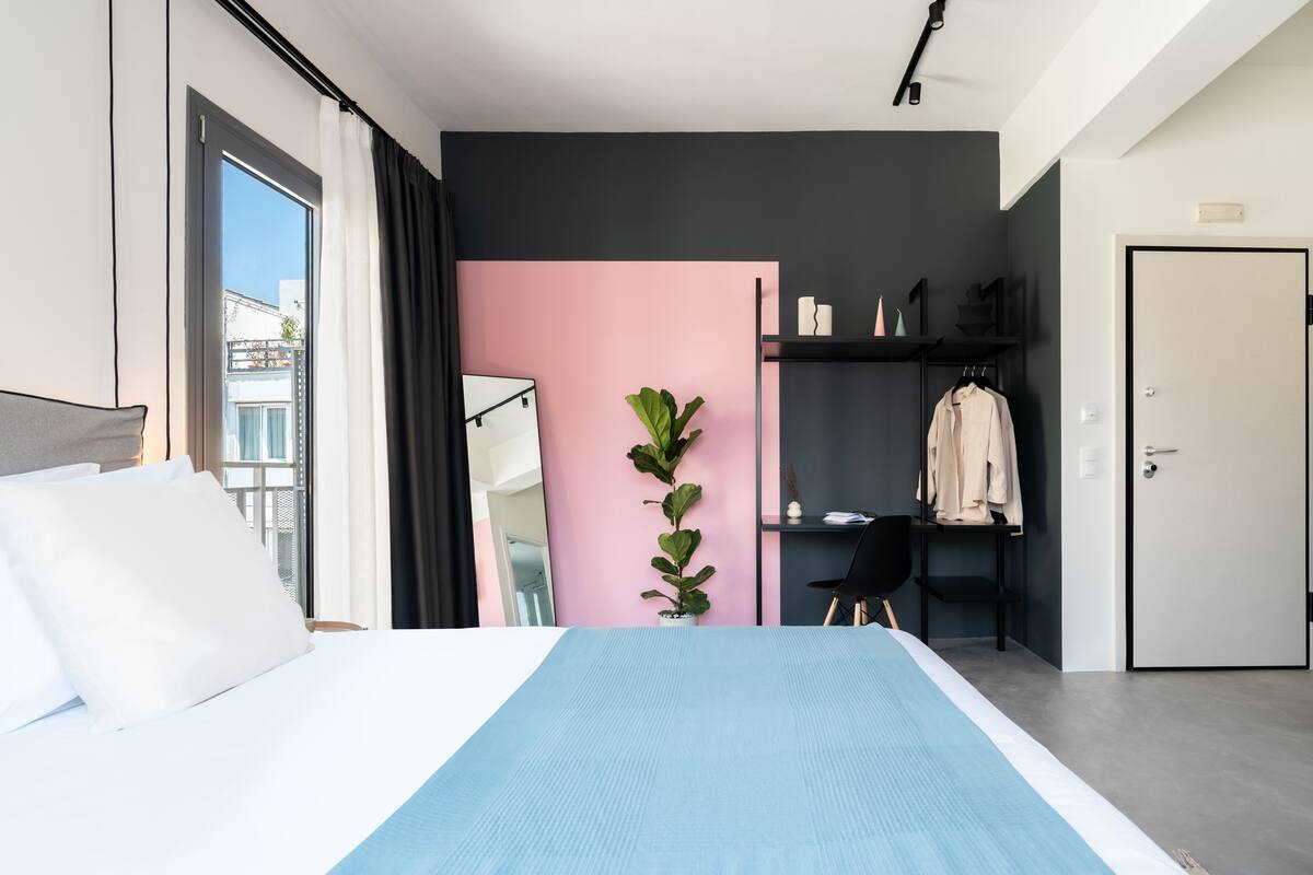 A modern hotel room with a large bed, a desk, a wardrobe, and a potted plant.