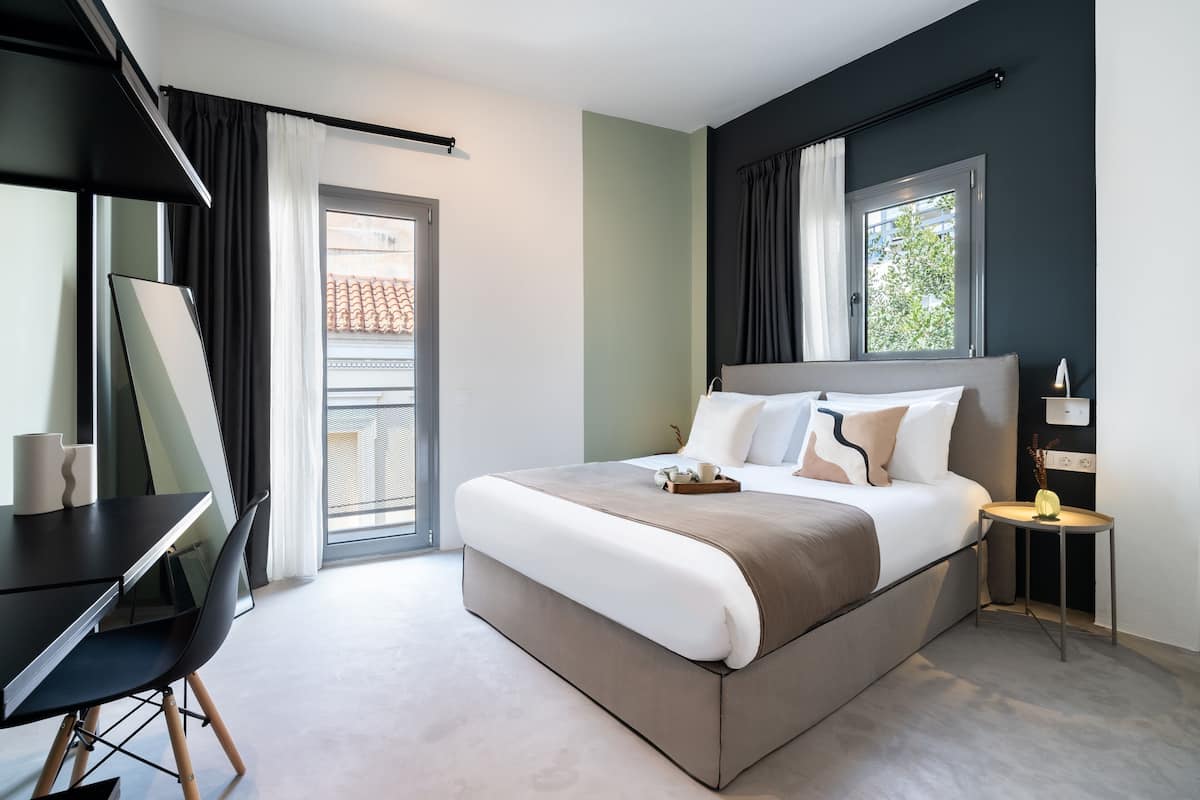 A modern hotel room with a large bed, a desk, and a small table with a lamp.