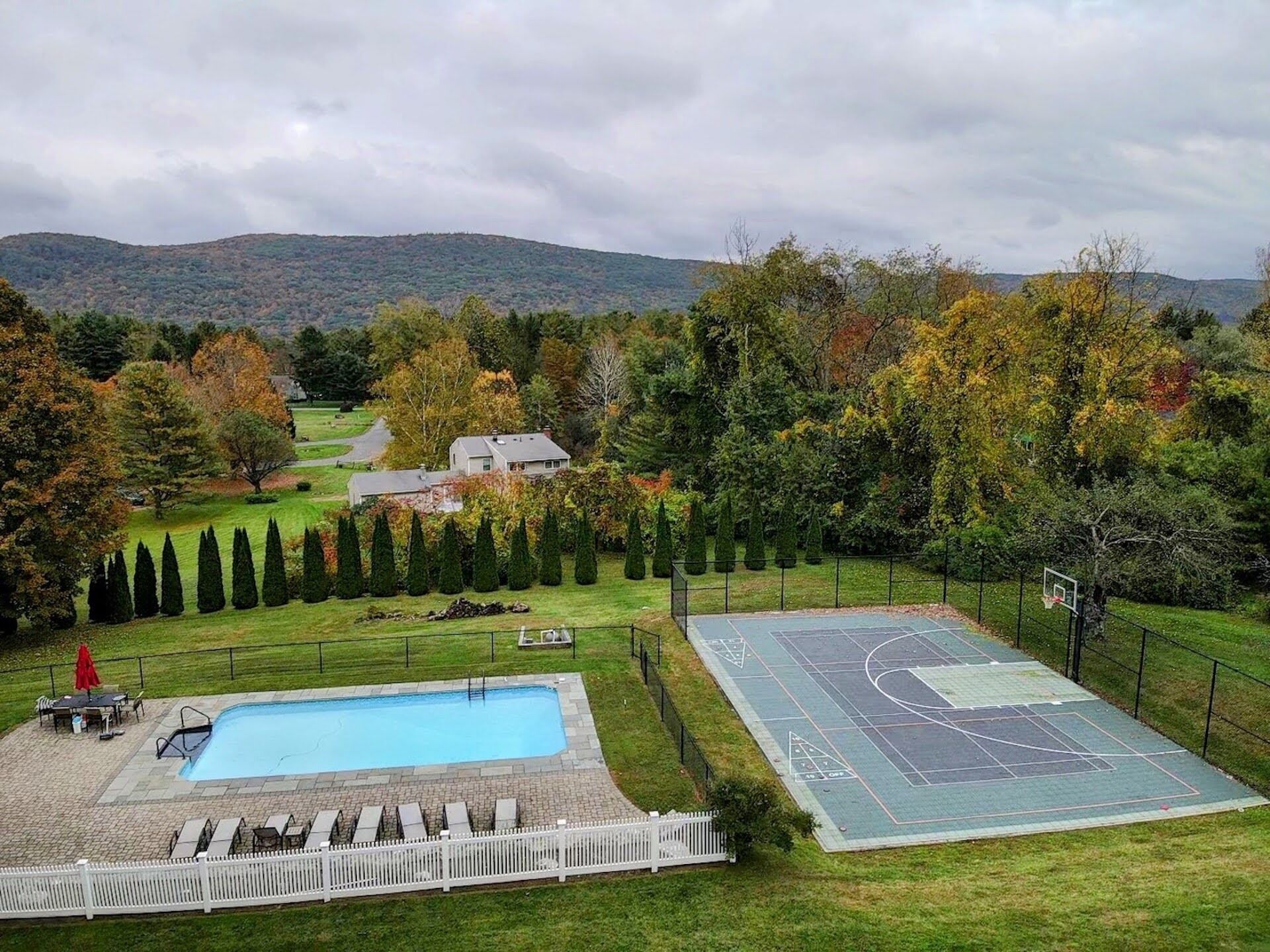 Zona residencial con piscina, cancha de baloncesto y una casa rodeada de árboles y colinas.