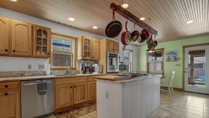A kitchen with wooden cabinets, a dishwasher, a large island, and hanging pots. - Family Tides-311 139th St-Bayside W/D, AC, WIFI (Ocean City)