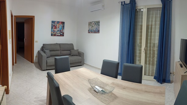 A dining area with a wooden table, four chairs, a sofa, and a TV on a wooden cabinet. - Vacation home byron (Contessa Entellina)