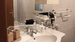 A modern bathroom with a large sink, mirror, and cabinet. There is a towel rack and a small table with cups and a bottle. - Vacation home byron (Contessa Entellina)