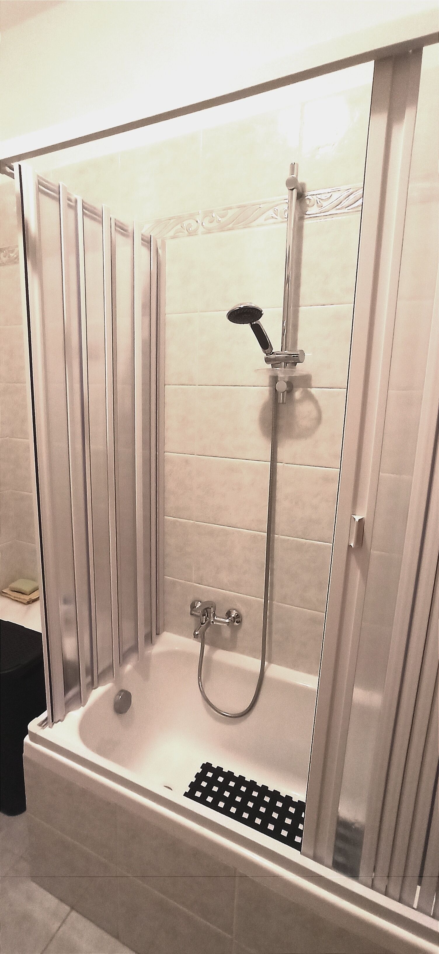 A walk-in shower with a glass door, a handheld showerhead, and a handheld faucet.