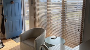 Eine Küche mit blauer Tür, einem grauen Sessel, einem kleinen runden Tisch und einem Fenster mit Holzjalousien.