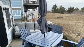 Eine Terrasse mit einem runden Tisch, vier Stühlen, einer Couch und einem Sonnenschirm.