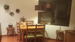 A dining area with a wooden table and chairs, a hanging light fixture, and a window with blinds.