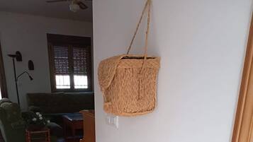 Una habitación con una cesta tejida colgada en la pared, un pequeño taburete con una planta y un aparador tejido junto a la pared.