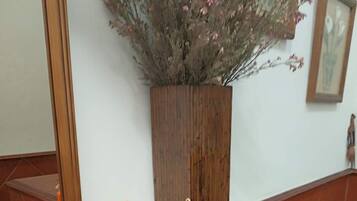 Dos velas sobre un suelo de baldosas, una jardinera de madera con flores, un espejo y una pequeña estatua.