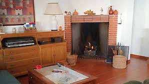 A living room with a fireplace, green sofas, a wooden coffee table, and a TV stand.