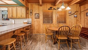 A rustic wooden cabin interior with a kitchen area featuring wooden cabinets, a dining table with chairs, and a bar stool area. - Enjoy a relaxing family retreat in this updated 3-bedroom, 2-bath cabin in Shaver Lake’s desirable East Village. (Shaver Lake)