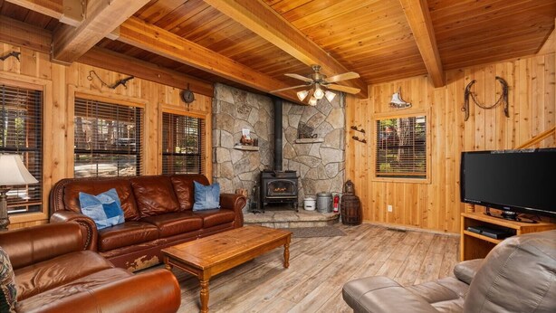 A cozy living room with a stone fireplace, leather sofas, a wooden coffee table, and a television. - Enjoy a relaxing family retreat in this updated 3-bedroom, 2-bath cabin in Shaver Lake’s desirable East Village. (Shaver Lake)