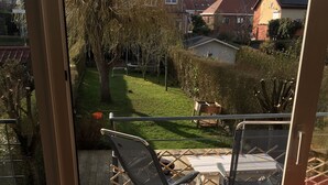 Un patio con dos sillas y una mesa, con vistas a un jardín y casas vecinas.
