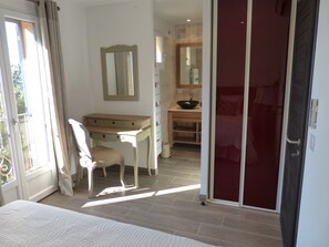 Een slaapkamer met een bed, een bureau, een stoel, een kaptafel met spiegel en een rode deur.