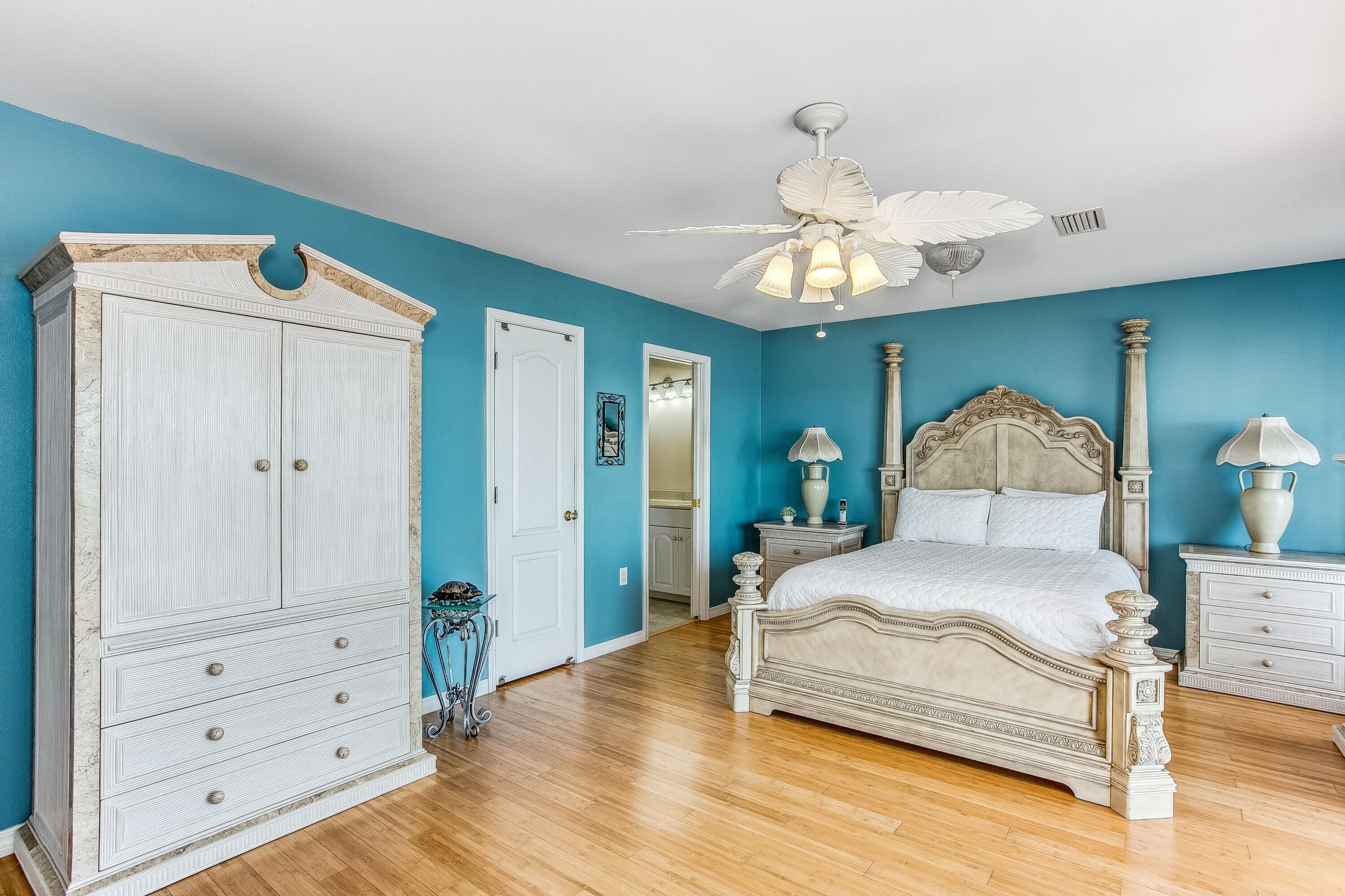 A bedroom with a large white wardrobe, a bed with a decorative headboard, and a ceiling fan.