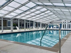 An indoor swimming pool with a glass ceiling, clear water, and a lifeguard stand.