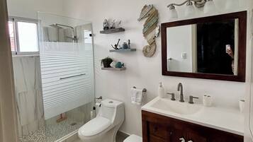 A modern bathroom with a glass-enclosed shower, a white toilet, a vanity with a mirror, and decorative wall shelves.
