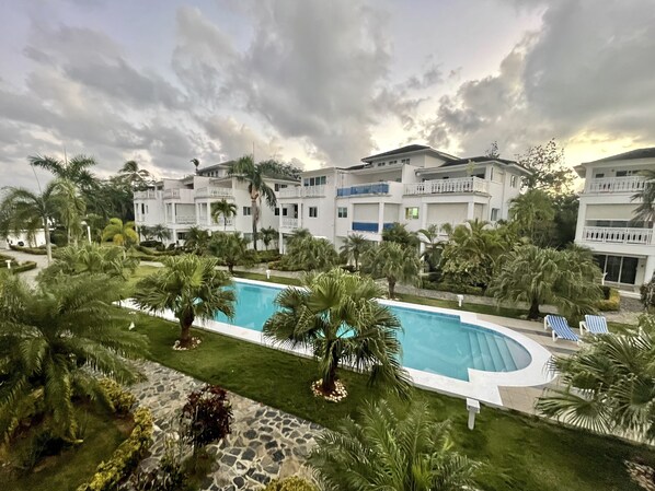 A resort with a swimming pool, palm trees, and a multi-story building with balconies.
