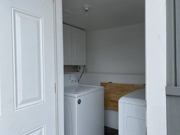 Ett tvättrum med tvättmaskin och torktumlare, träskåp och en vit dörr.