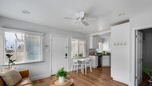 A modern living room with a sofa, a round coffee table, and a ceiling fan. There is a kitchen area with white cabinets and a dining table. - OCEAN VIEW|Steps to the Beach, Main St. & Pac City (Huntington Beach)