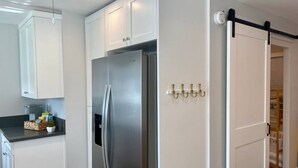 A modern kitchen with white cabinetry, a stainless steel refrigerator, and a sliding door closet. - Steps To Beach, Main St, Pac City | BBQ | Firepit (Huntington Beach)
