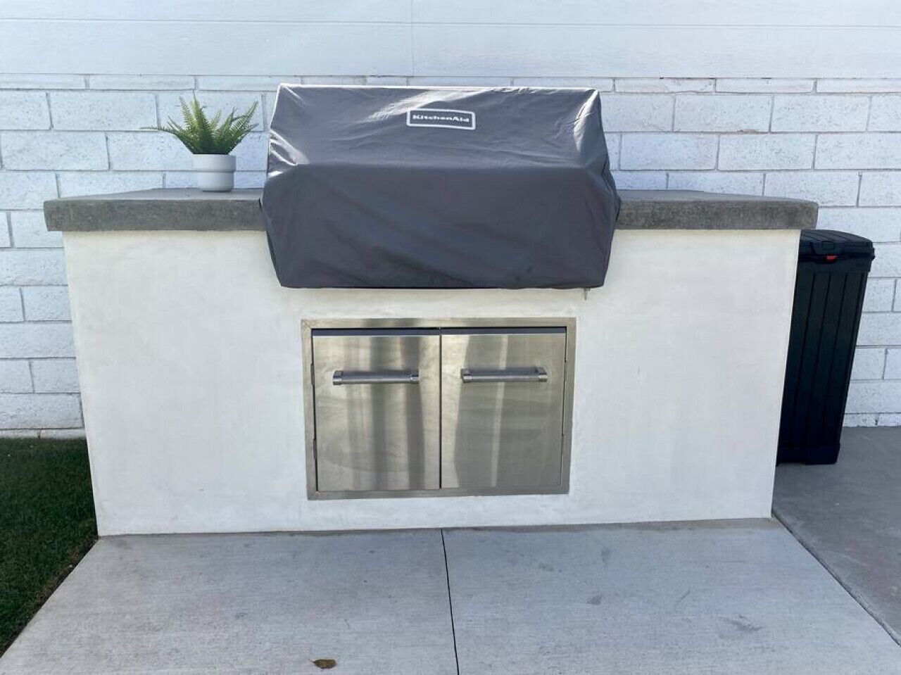 A kitchen area with a built-in grill, a potted plant, and a trash can.