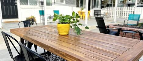 Une table en bois avec des chaises, un pot de fleurs jaune contenant une plante et un tapis à motifs.