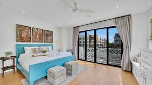 Un dormitorio con una cama grande, un ventilador de techo y vistas de la ciudad a través de una puerta corrediza de vidrio.