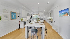 A modern kitchen with white cabinetry, a central island with stools, and a view of the dining area. - Rooftop Ocean Views / 2min Walk To Beach / Private Pool (Huntington Beach)