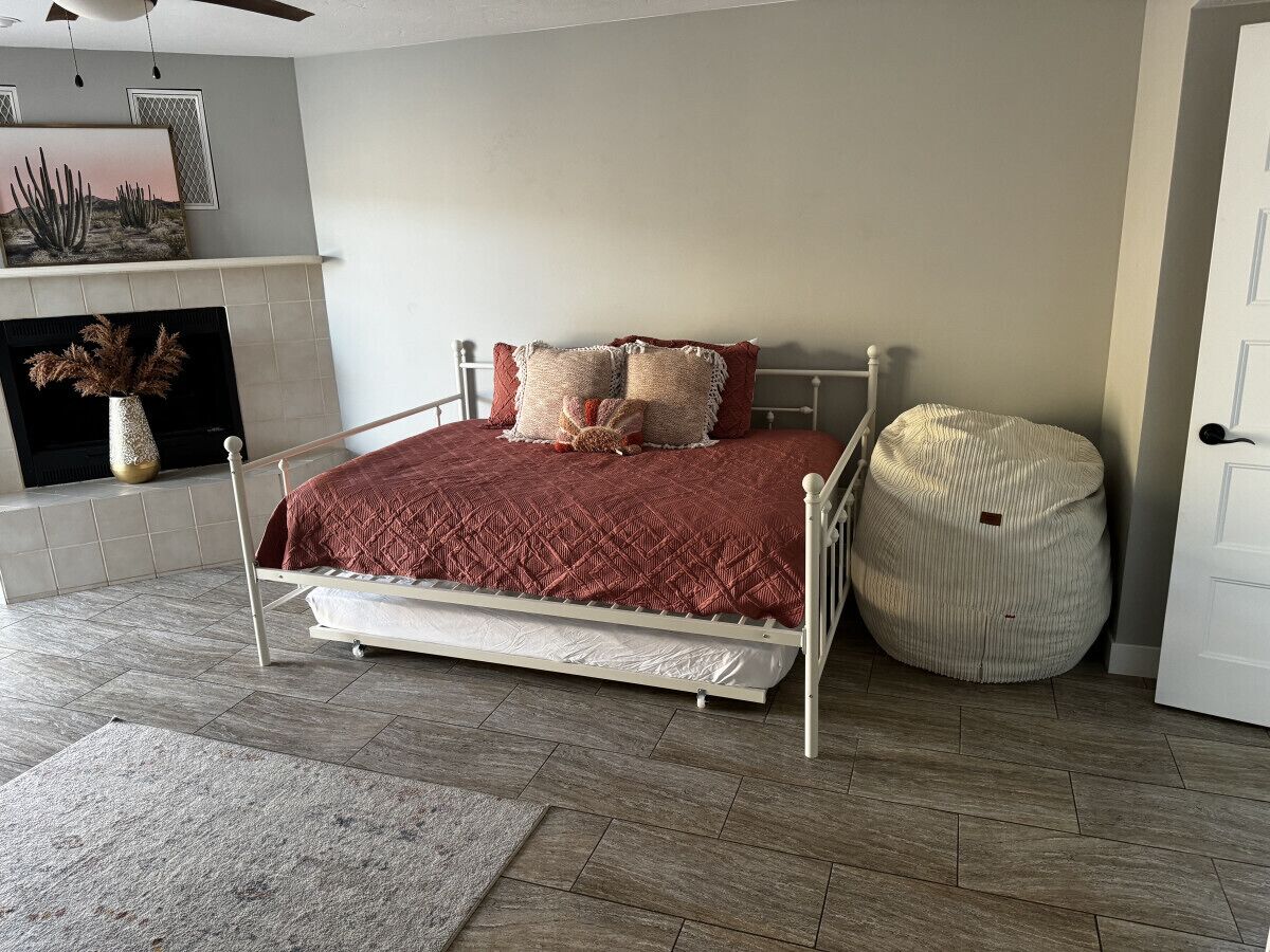 A bedroom with a bed, pillows, a bedside table, a chair, a rug, and a fireplace.