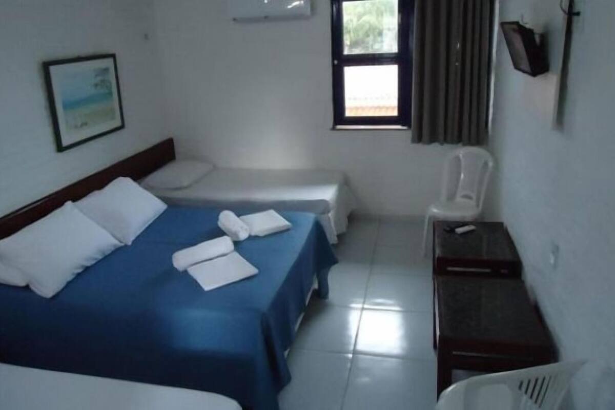 A hotel room with two beds, a chair, a small table, and a window with curtains.