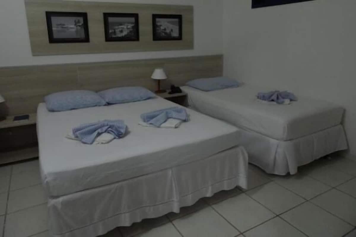 A hotel room with two beds, each with a pillow and a blanket. There are three framed pictures on the wall above the beds.