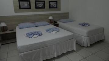 Une chambre d’hôtel avec deux lits, chacun étant équipé d’un oreiller et d’une couverture. Trois tableaux encadrés sont accrochés au mur au-dessus des lits.