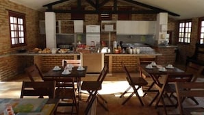 A rustic kitchen with brick walls, wooden beams, and a central island with a sink and counter space. There are dining tables with chairs arranged around the kitchen. - Hotel Praia do Futuro (Fortaleza)
