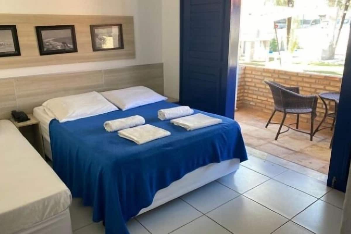 A hotel room with a large bed, a smaller bed, a desk with a phone, and a chair by the window.